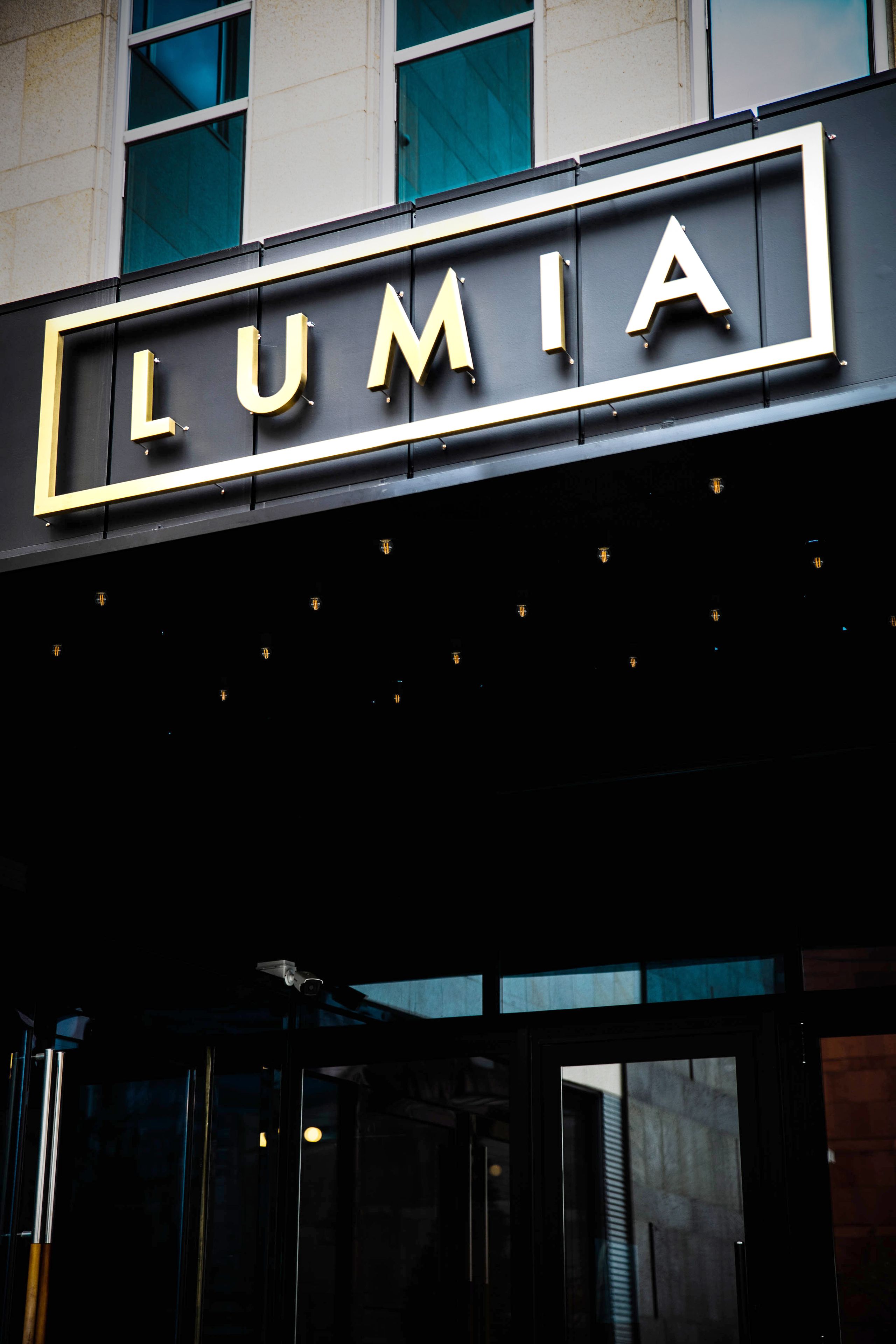 A building entrance with the sign "LUMIA" in gold letters on a black background.