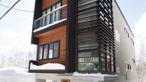 A modern multi-story building with a wooden facade and large windows, surrounded by snow. - Tamo (Kutchan)