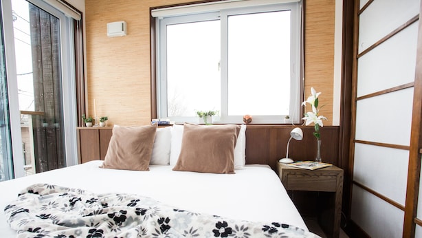 A hotel room with a bed, a nightstand, a window, and a view of the outside. - Tamo (Kutchan)