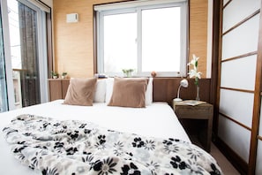 A hotel room with a bed, a nightstand, a window, and a view of the outside. - Tamo (Kutchan)