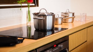 A kitchen with a black induction cooktop, stainless steel pots, a glass vase with flowers, and wooden cabinets. - Tamo (Kutchan)