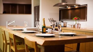 A modern kitchen with a long island counter, equipped with a bottle of champagne, glasses, and a vase with a flower. - Tamo (Kutchan)