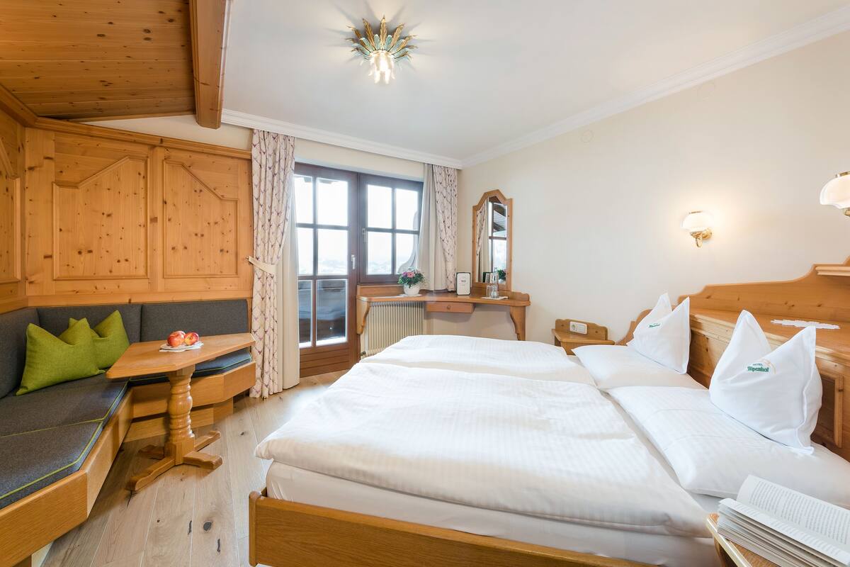 A hotel room with a wooden ceiling, a sofa with green cushions, a wooden table with apples, and two beds with white bedding.