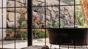 Ein Zimmer mit Blick durch ein Fenster, eine Steinsäule, ein Korbstuhl und Holzboden.