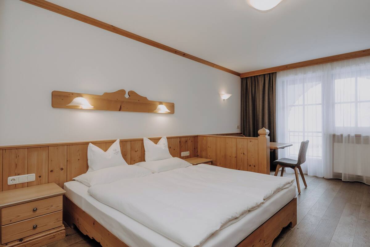 A bedroom with a wooden bed, a nightstand, a desk, and a chair.