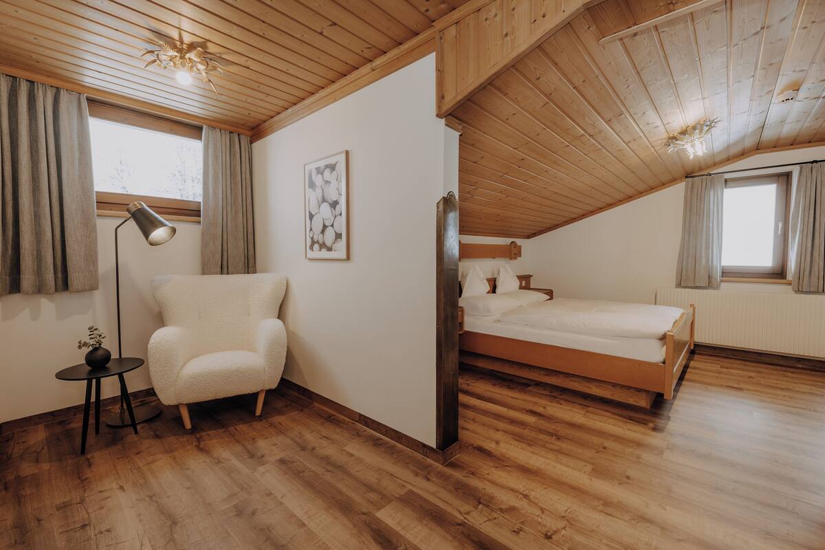 A bedroom with a wooden ceiling, a bed, a chair, a lamp, and a window.