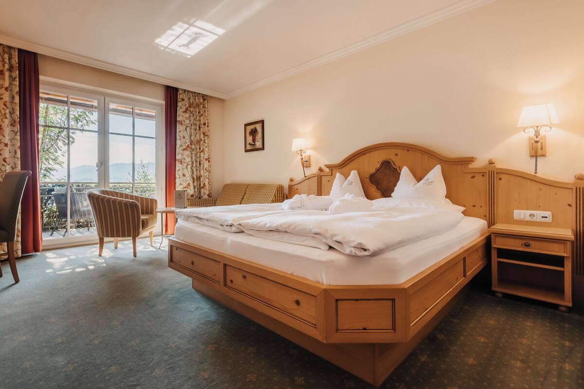 A hotel room with a large bed, a chair, a desk, and a view of the outdoors through a sliding door.