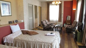 A hotel room with two beds, a small table, two armchairs, a chair, a mirror, and a lamp. - Hotel Platon (Chikuma)