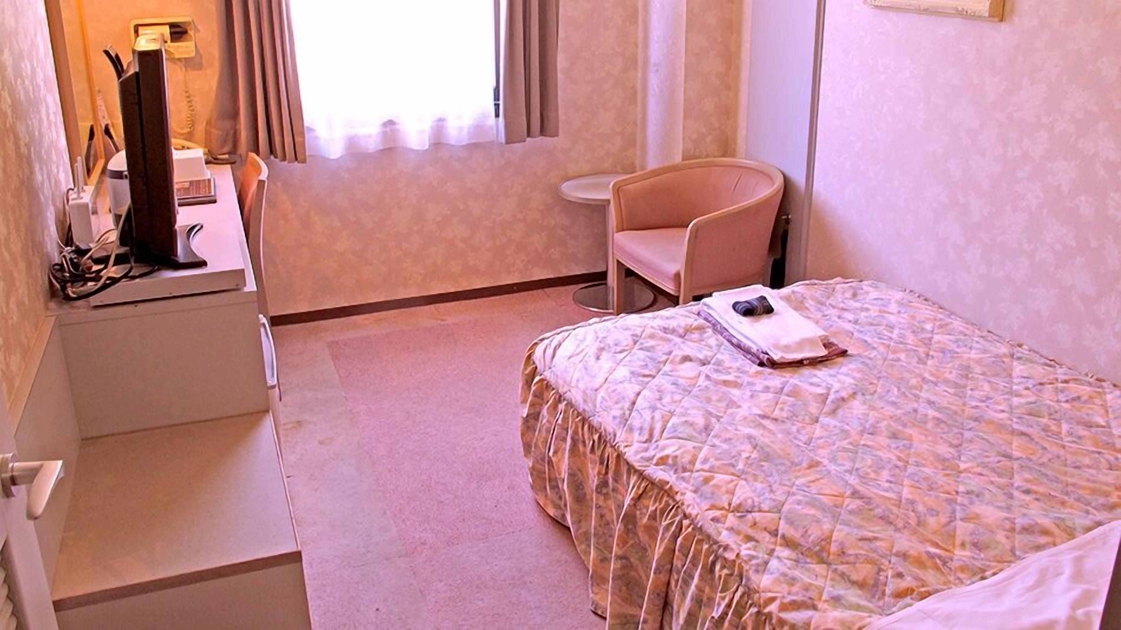 Quarto de hotel com cama, escrivaninha, cadeira e mesa pequena.