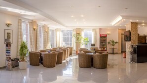 A spacious lobby with a high ceiling, large windows, and a Coca-Cola refrigerator. - Hotel West (Bratislava)