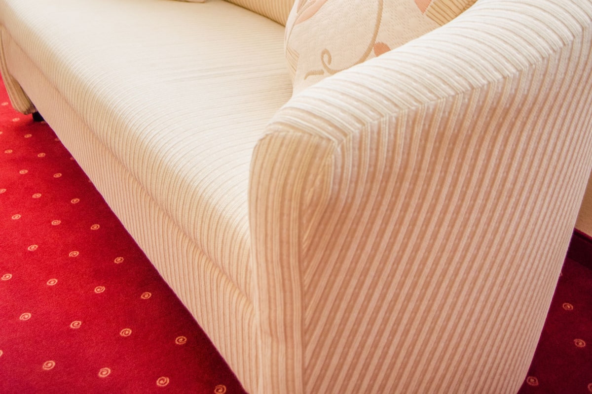 Um sofá bege com almofadas estampadas de flores, um tapete vermelho com padrão e cortinas leves.