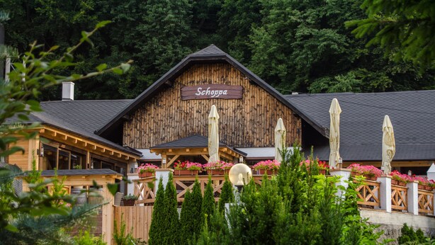 A wooden chalet with a sign reading "Schogga." It features a balcony with potted plants and umbrellas. - Hotel West (Bratislava)