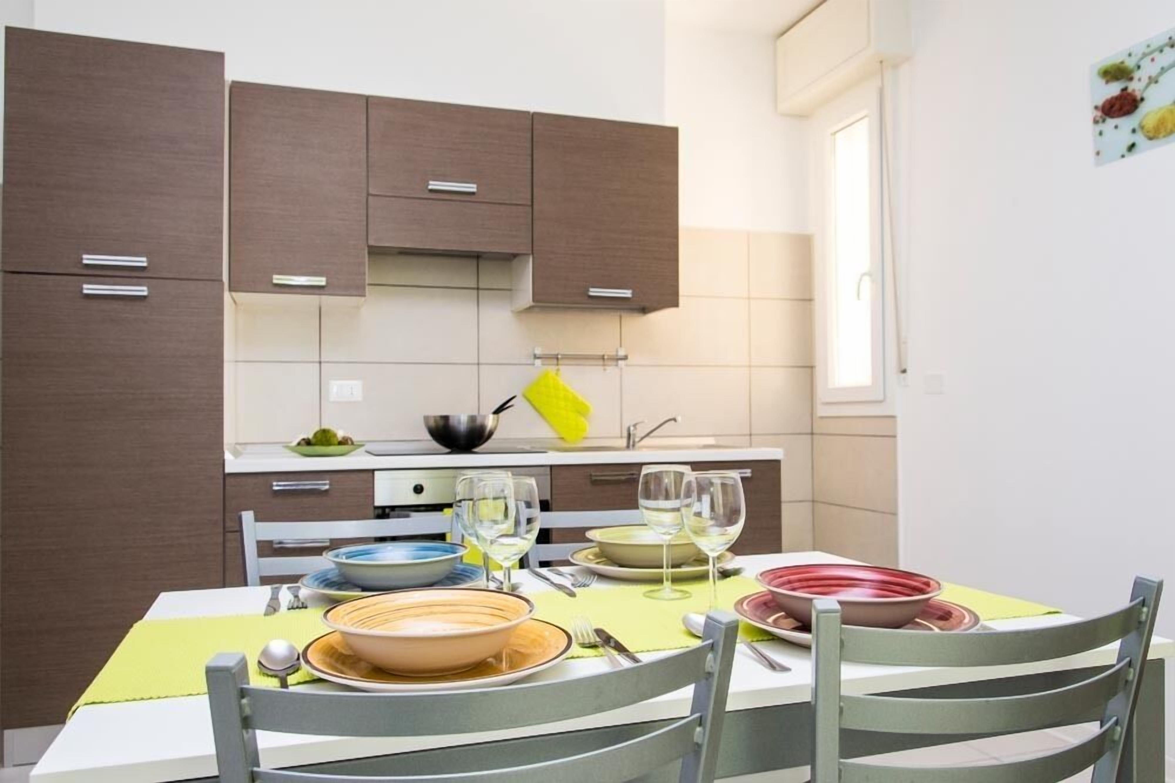 Una cucina moderna con mobili marroni, un tavolo da pranzo apparecchiato con piatti, ciotole e bicchieri da vino.