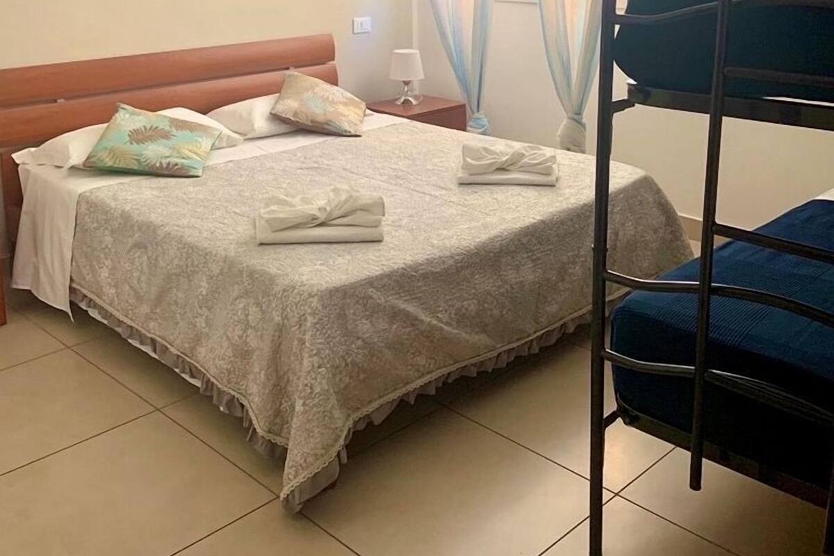 Een hotelkamer met een bed, nachtkastje, lamp, raam met gordijnen en een stapelbed.