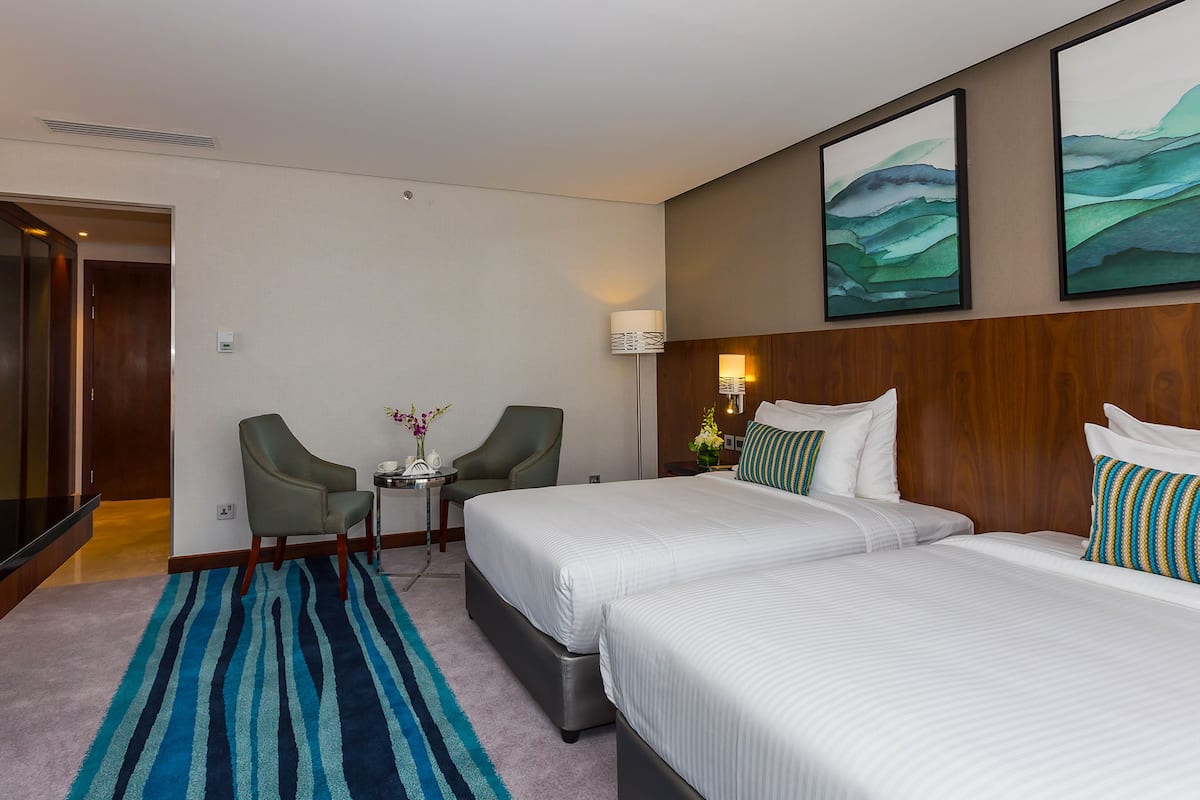 Una habitación de hotel con dos camas, una mesita con un florero y una silla.