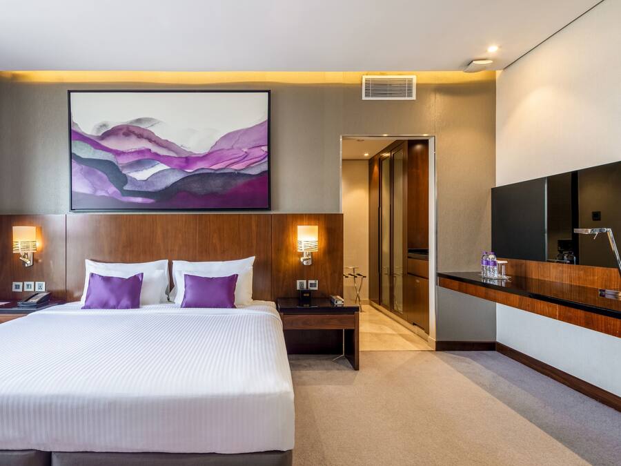 Una habitación de hotel con una cama grande, un escritorio, un espejo y un cuadro en la pared.