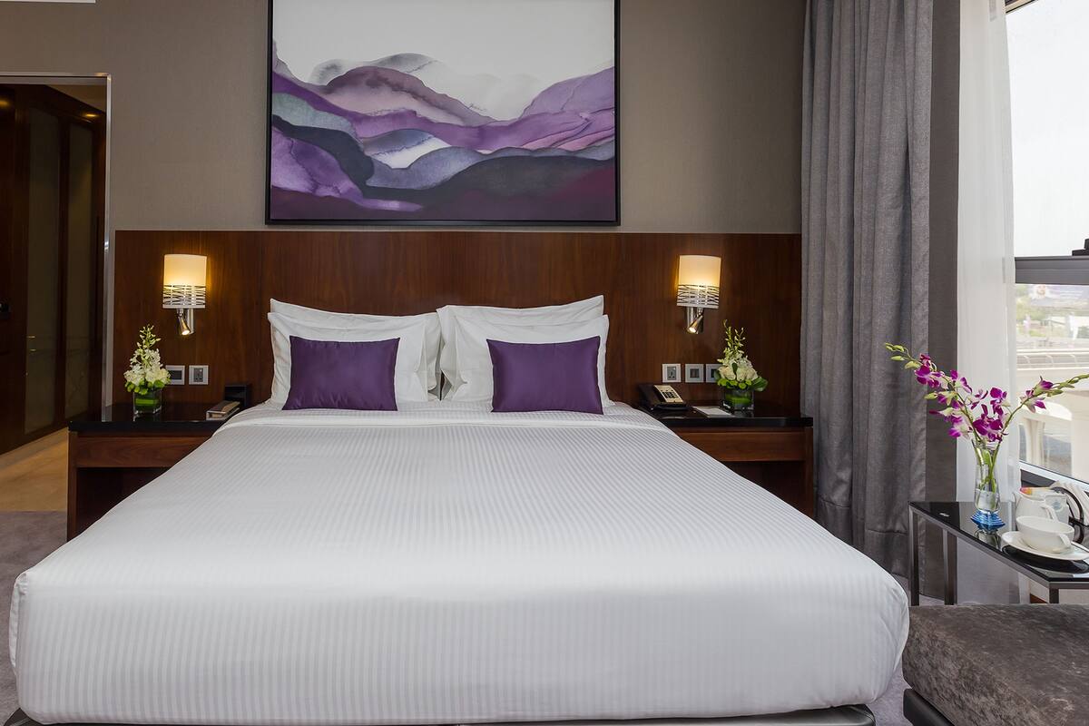 Habitación de hotel con una cama grande, dos mesitas de noche, una lámpara de pared y una ventana con cortinas.