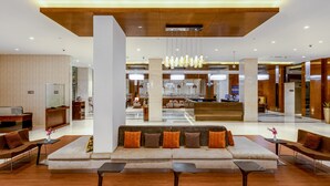 Un hall d’hôtel moderne avec un espace salon central, un comptoir d’accueil et, au fond, un espace repas.