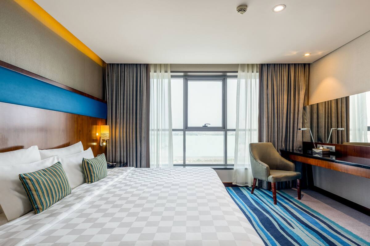 Habitación de hotel con una cama grande, un escritorio, una silla y vistas al mar.