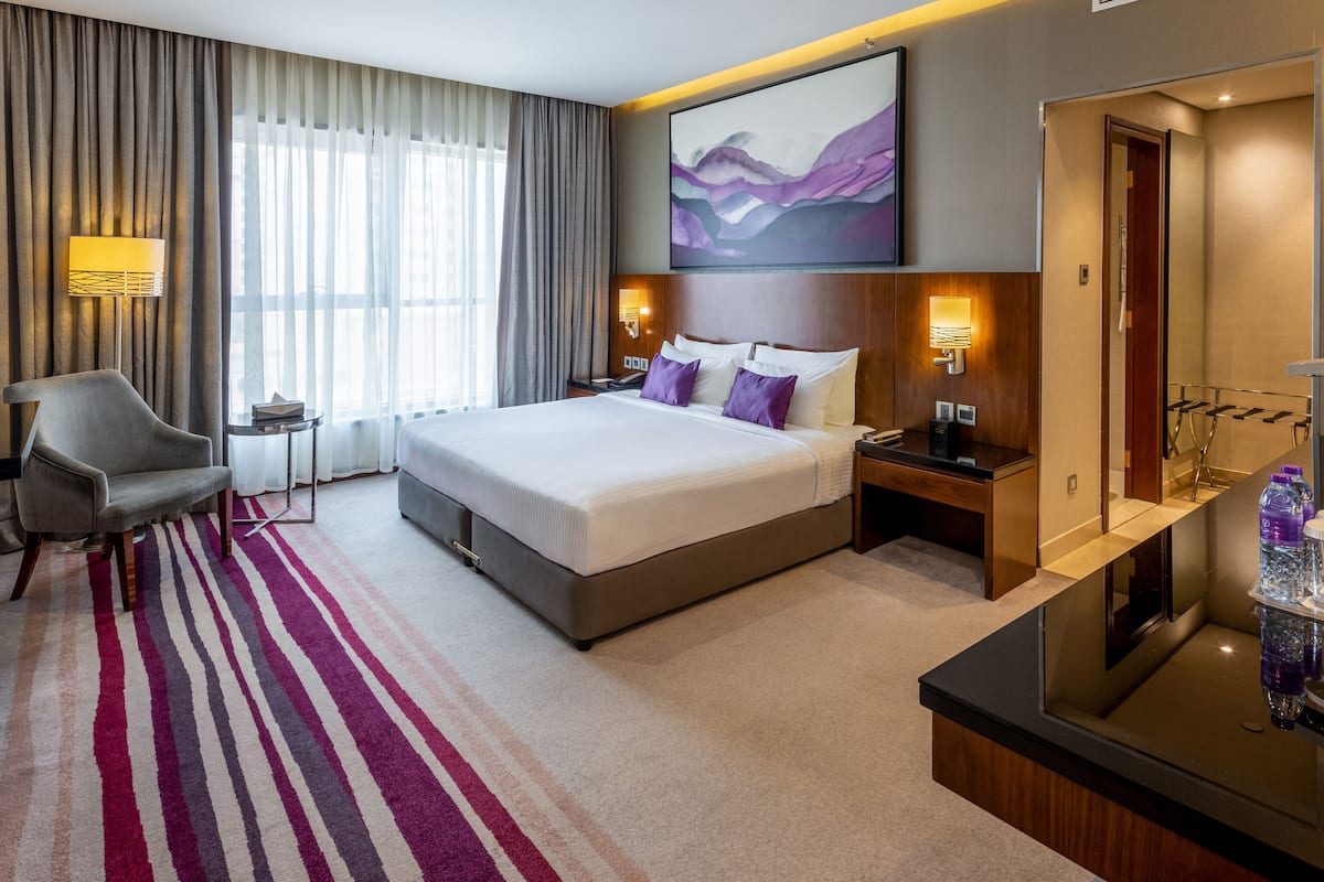 Habitación de hotel con una cama grande, un escritorio, una silla, una tocador con espejo y una ventana con cortinas.