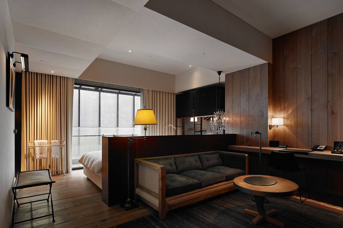 A modern hotel room with a bed, a sofa, a desk, and a small round table.