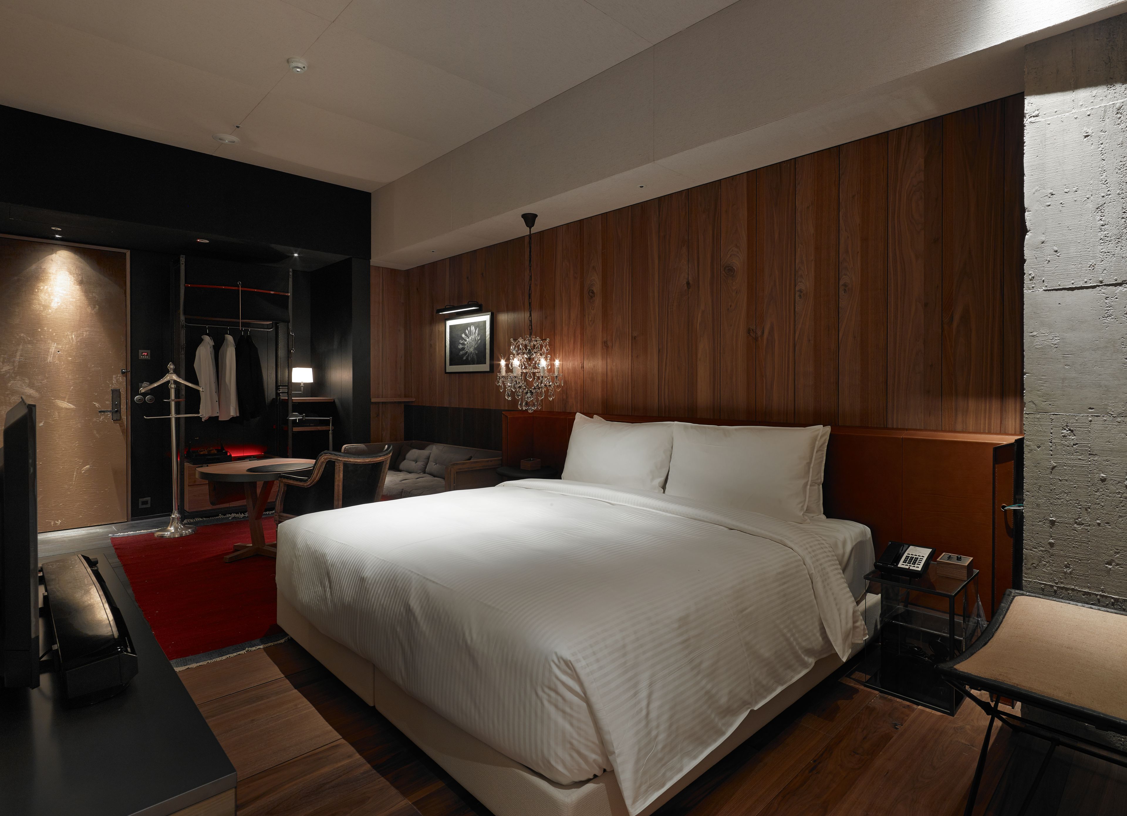 A modern hotel room with a large bed, a desk with a chair, a wardrobe, and a red carpet.