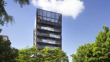 Un immeuble moderne à plusieurs étages, doté de balcons et de grandes fenêtres, entouré d’arbres verdoyants.