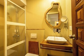 A bathroom with a wooden vanity, a large mirror, a white sink, and a shower enclosure.