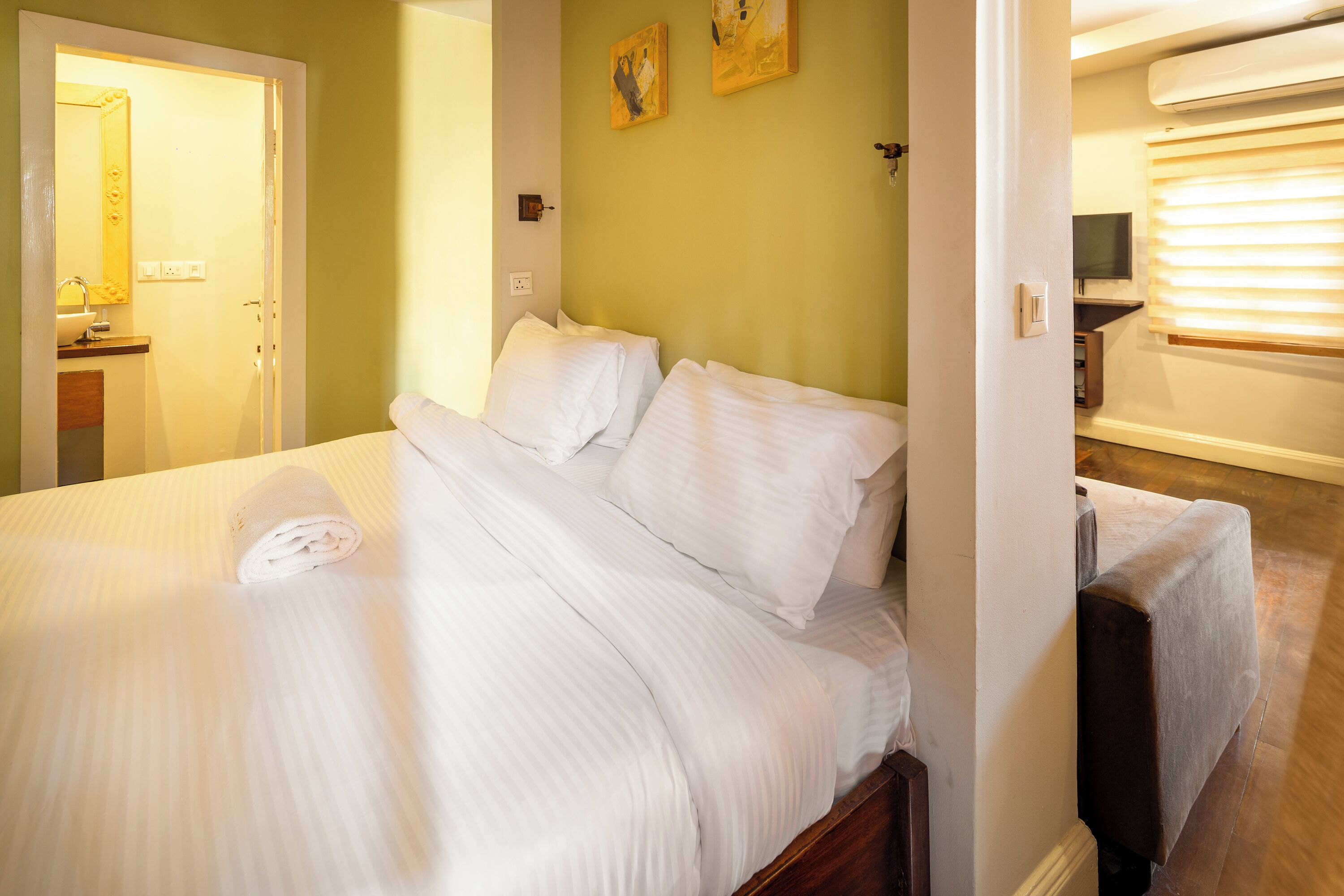 A neatly made bed with white linens and pillows, a wooden headboard, and a small bedside table with a lamp.