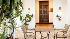 A patio with a table and chairs, a potted plant, and a wooden door with a decorative panel. - Olma Hotel & Suites (Accra)