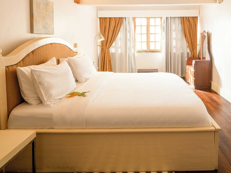 Un lit bien fait, avec du linge de lit blanc et une tête de lit en bois, une table de chevet et une commode avec des tiroirs.
