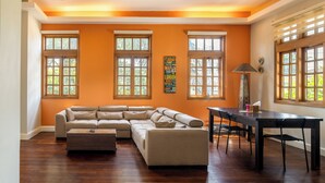 A living room with a sectional sofa, a dining table with chairs, and large windows with blinds. - Olma Hotel & Suites (Accra)