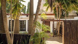 A courtyard with palm trees, a bamboo fence, and a building with windows and a door. - Olma Hotel & Suites (Accra)