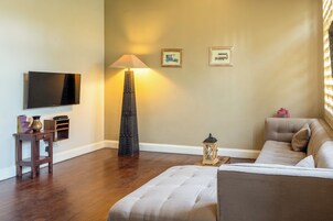 Un salon équipé d’un téléviseur à écran plat, d’un grand lampadaire, d’un canapé et de deux tableaux encadrés accrochés au mur.
