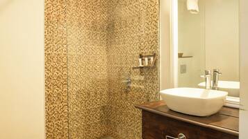Un baño con pared de ducha en mosaico, un lavamanos blanco y un mueble de tocador de madera.