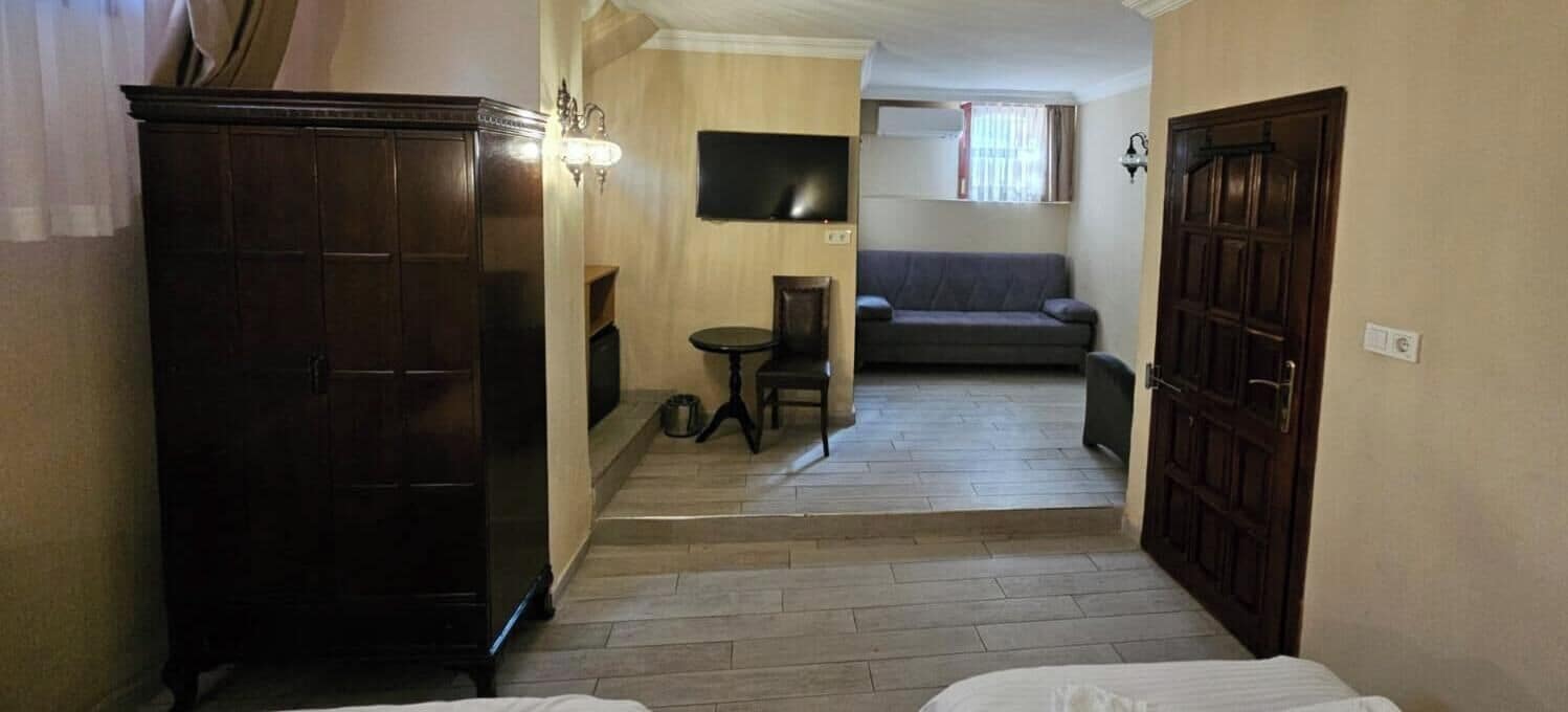 Un couloir étroit avec une armoire en bois, une petite table avec une chaise, un canapé et un téléviseur fixé au mur.