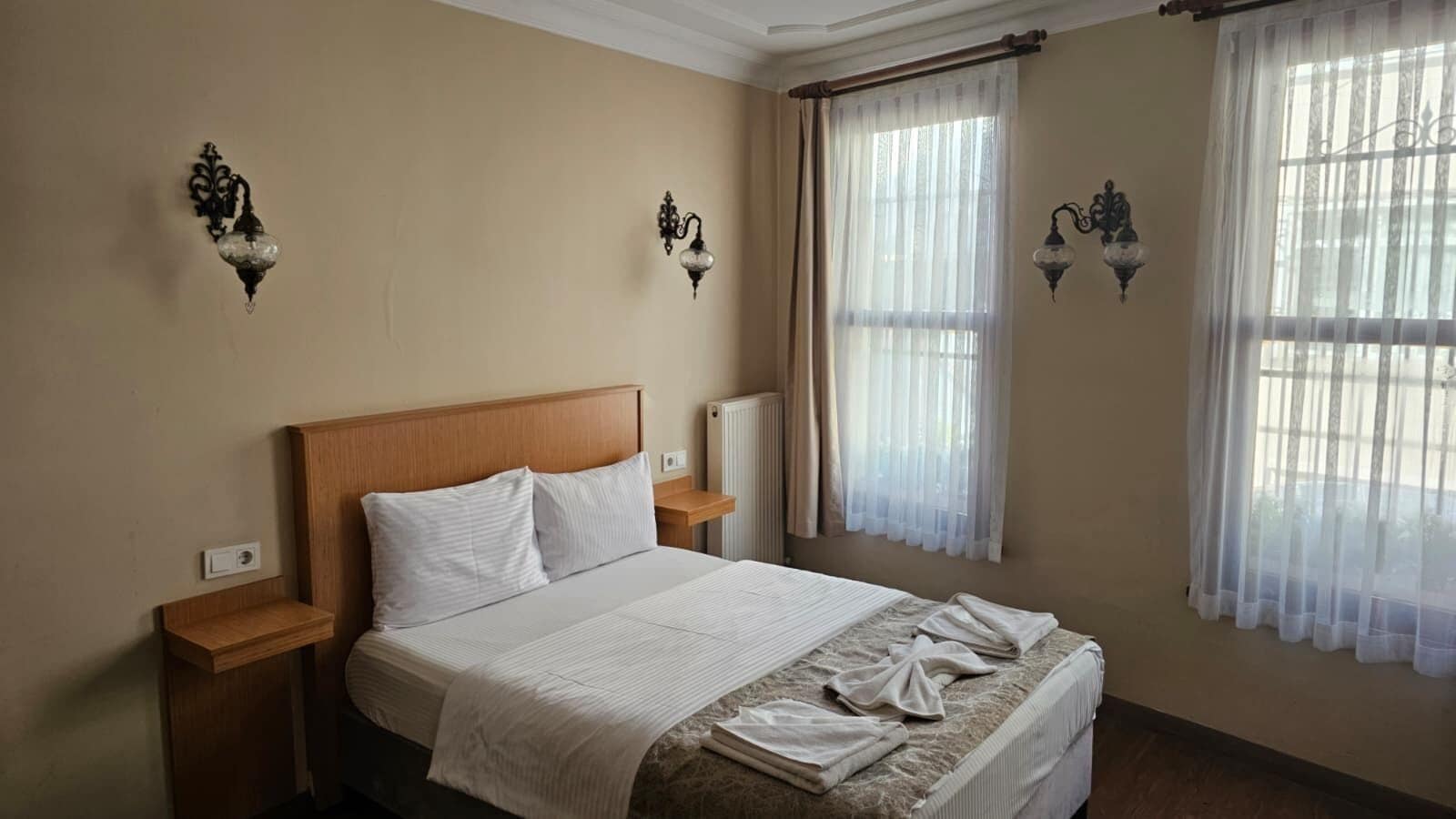 A neatly made bed with white linens, two bedside tables, and wall-mounted lamps.