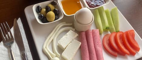 A breakfast tray with bread, cheese, ham, tomatoes, olives, and a glass of tea.