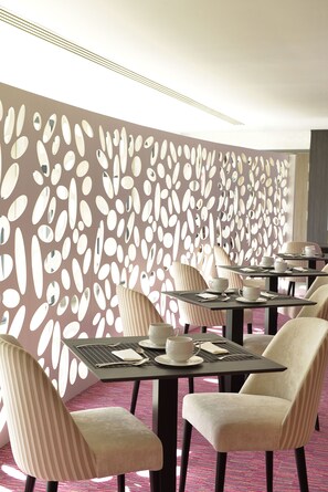 Un espace repas avec des tables et des chaises, un mur décoratif orné de motifs découpés et un sol recouvert de moquette.