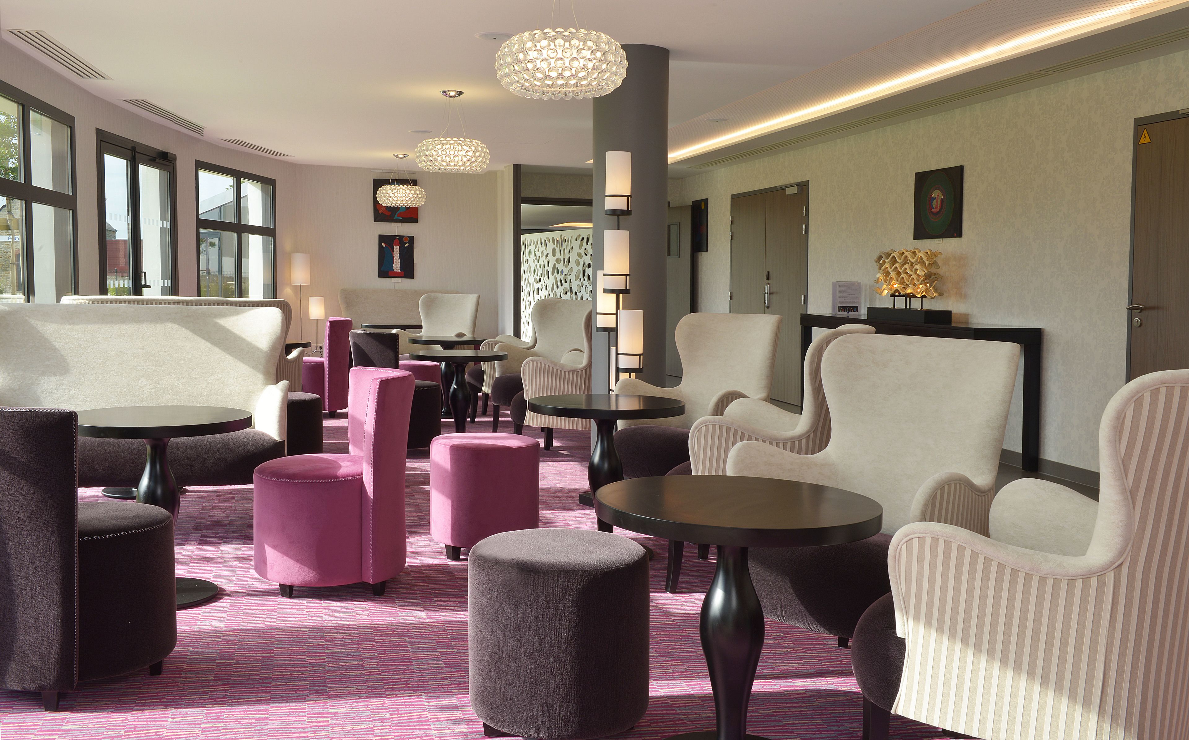 Un espacio lounge moderno con diversas opciones de asientos, como sillones y otomanas, una alfombra estampada y lámparas de diseño contemporáneo.