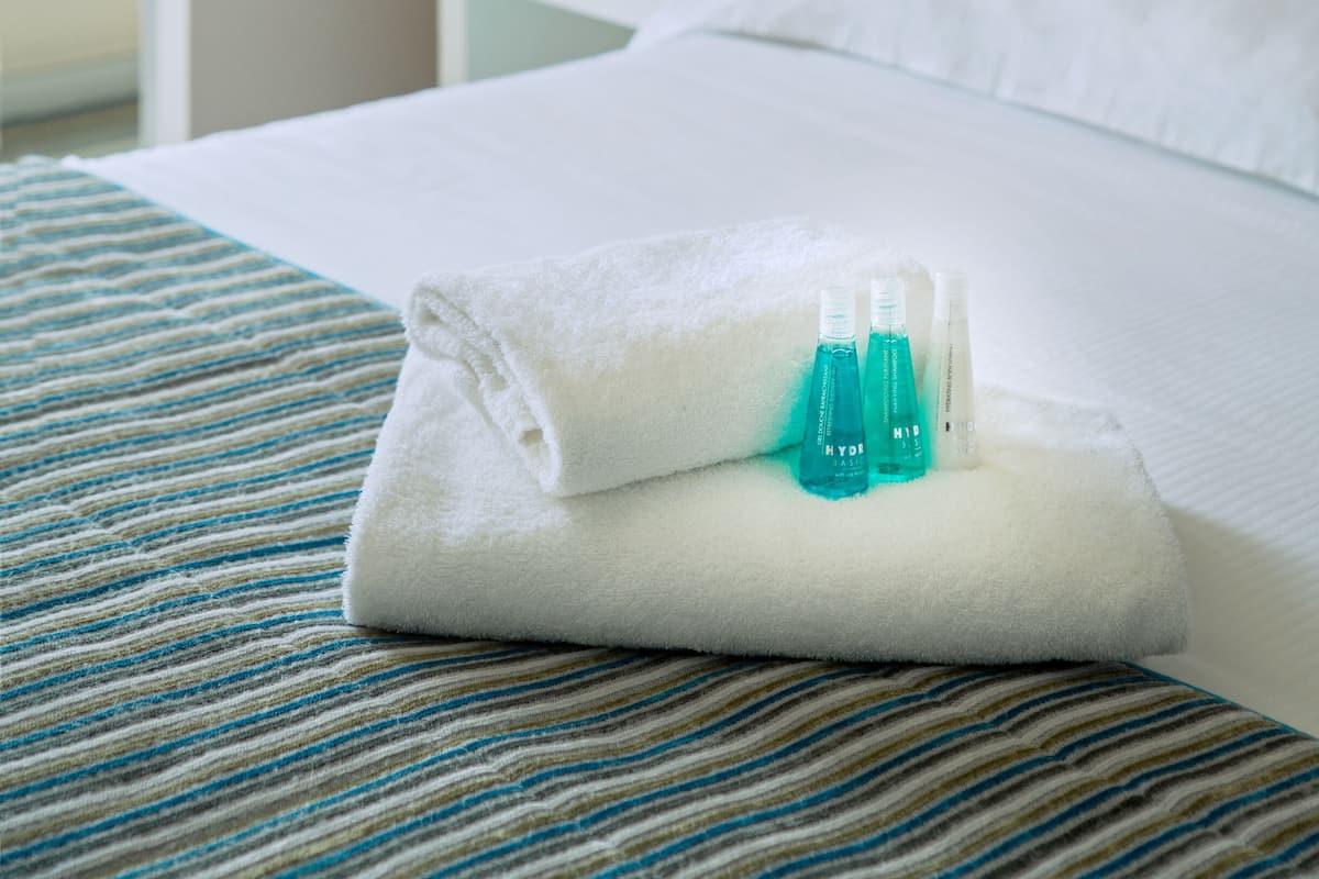 A neatly made bed with a folded white towel and two bottles of toiletries.