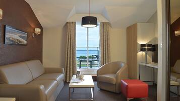 Une chambre d’hôtel équipée d’un canapé, d’un fauteuil, d’un pouf et d’une petite table avec une lampe.
