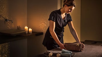 Een spa-omgeving met een massagetafel, kaarsen en een handdoek met een zeester.