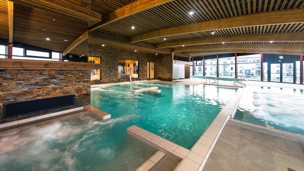 Una piscina interior con pared de piedra y vigas de techo de madera.