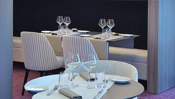 A restaurant with a modern interior, featuring a seating area with tables and chairs, a large illuminated sign above the entrance, and a patterned carpet.