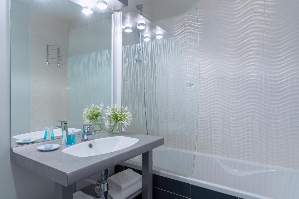 A modern bathroom with a large mirror, a sink, and a shower area.