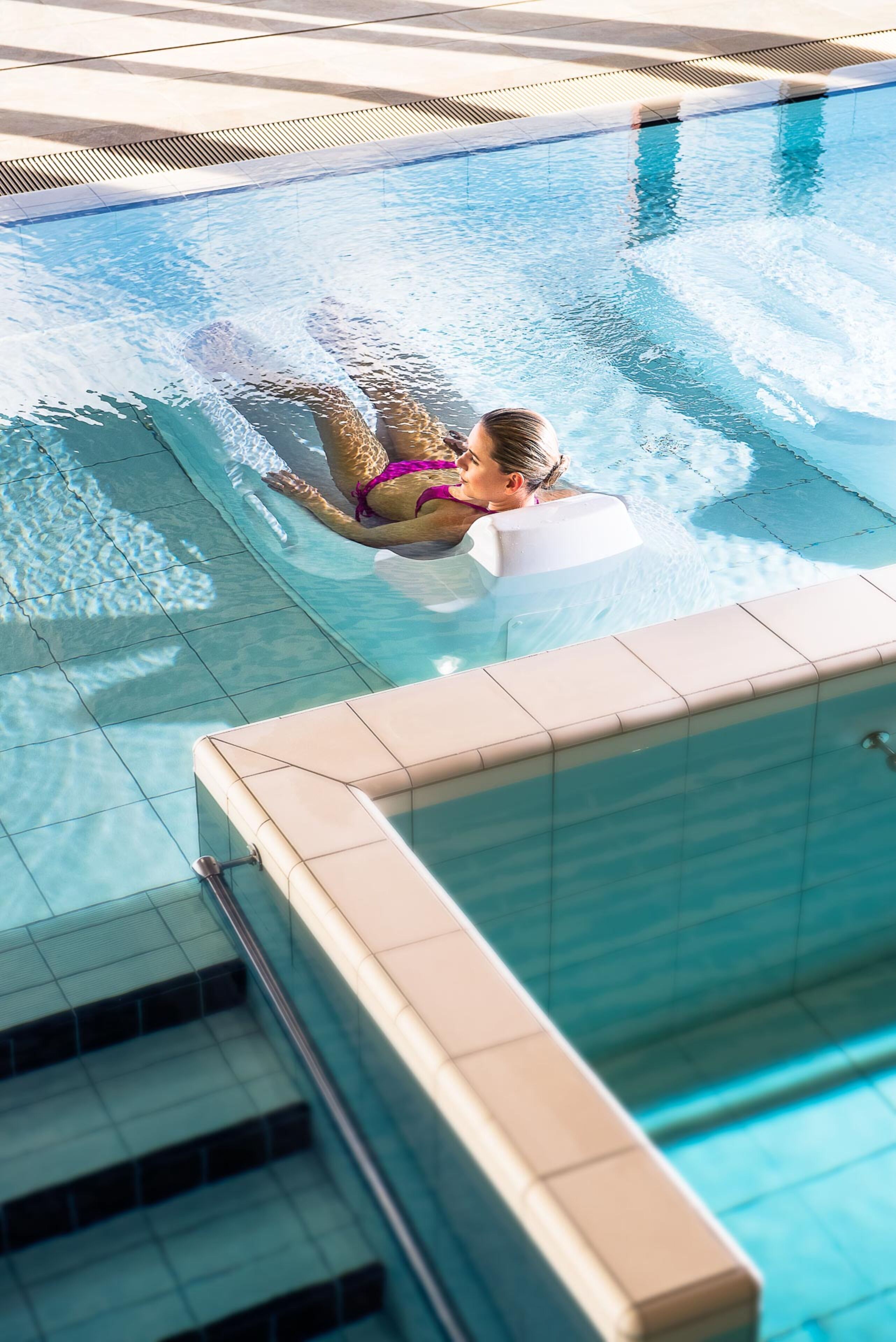 A swimming pool with clear water, a tiled deck, and a pool ladder.