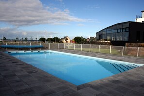 A rectangular swimming pool with a tiled deck, surrounded by a fence and a building with large windows. - Thalasso Concarneau Spa Marin Resort (Concarneau)