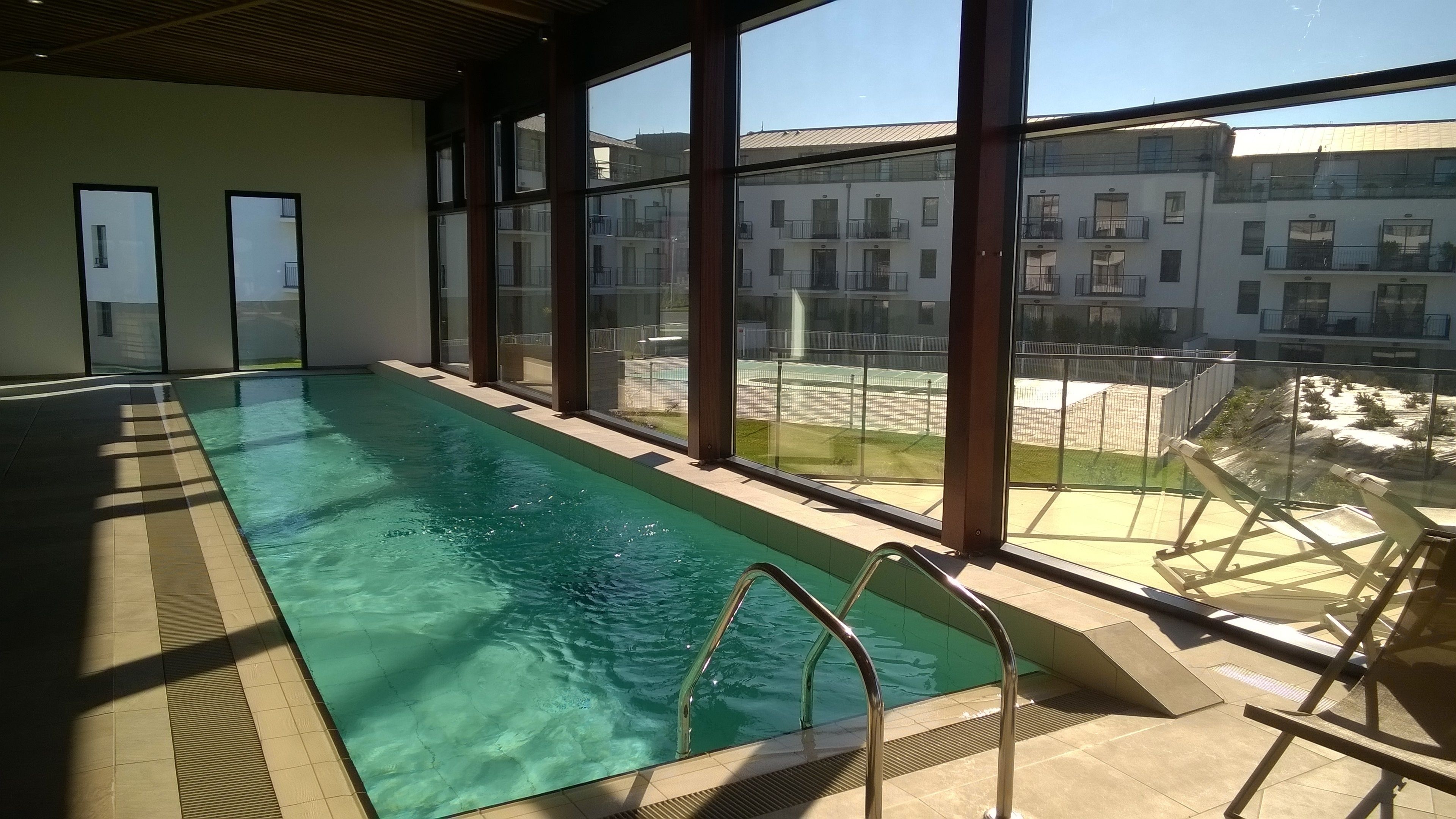 An indoor swimming pool with clear water, large windows, and a view of a residential area.