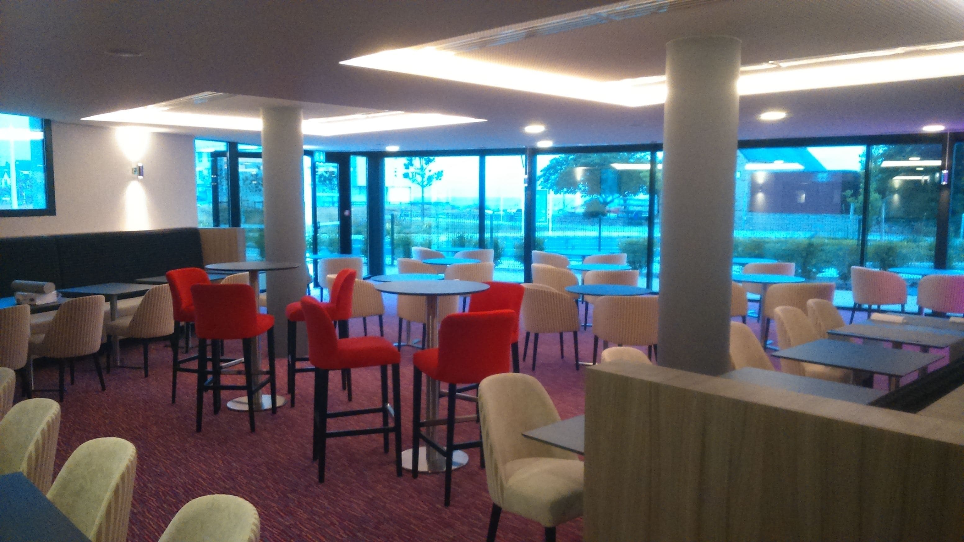 Een moderne eetruimte met ronde tafels en stoelen, grote ramen en uitzicht op de omgeving.